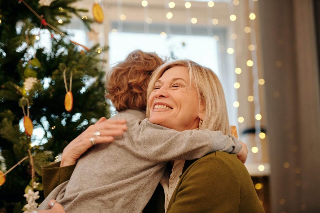 Young boy hugging his grandmother in a cozy, festive setting with a Christmas tree and warm lights, symbolizing family connection and warmth.