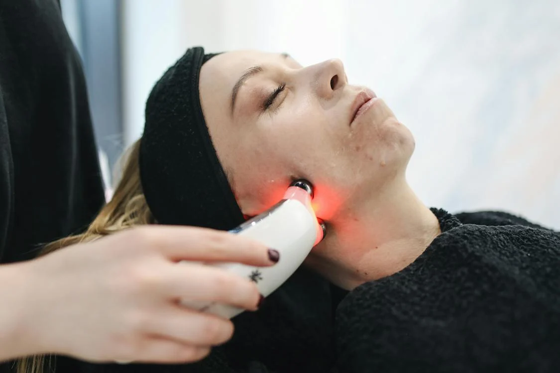 Woman receiving Lumecca IPL treatment on her face, with a handheld device emitting red light, in a serene clinical setting.
