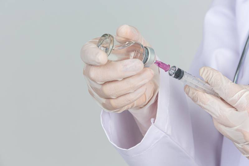 Young healthcare professional in gloves preparing a hypodermic syringe with a vaccine vial, emphasizing peptide therapy's role in immune support and overall health.