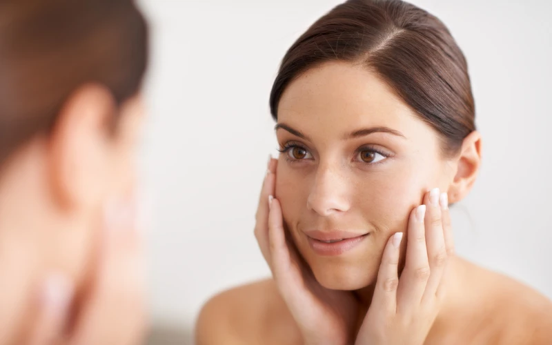Woman examining her skin post-Morpheus8 facial rejuvenation treatment, showcasing improved texture and radiance.